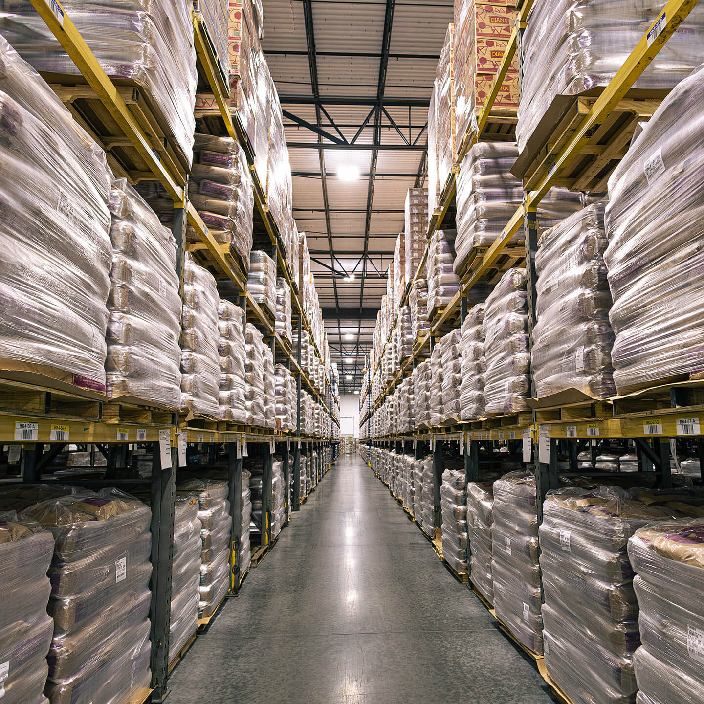 Narrow aisle of a large warehouse with high-density inventory storage racks.