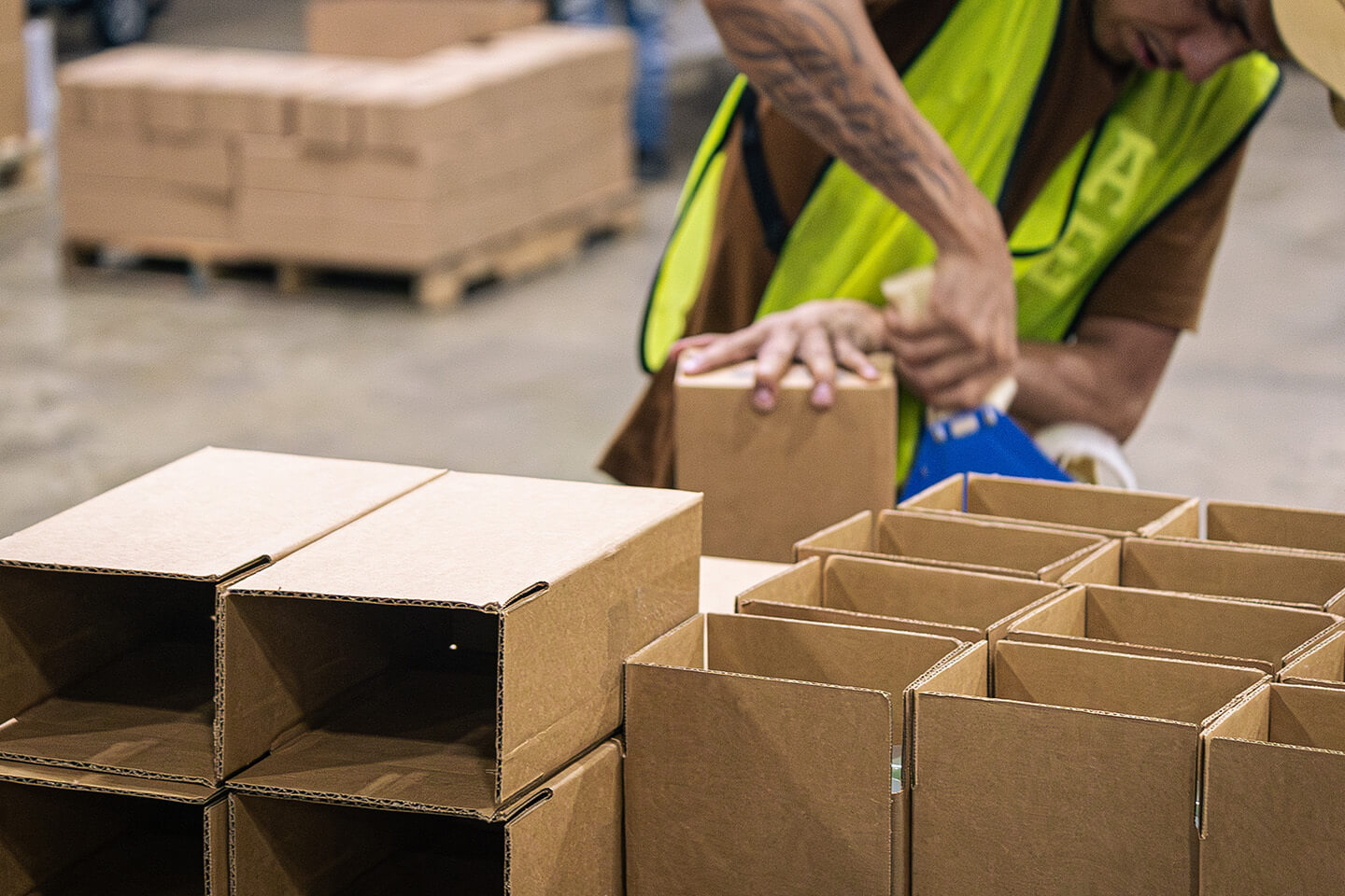 Logistics worker using a tape gun to assemble cardboard boxes for shipment.