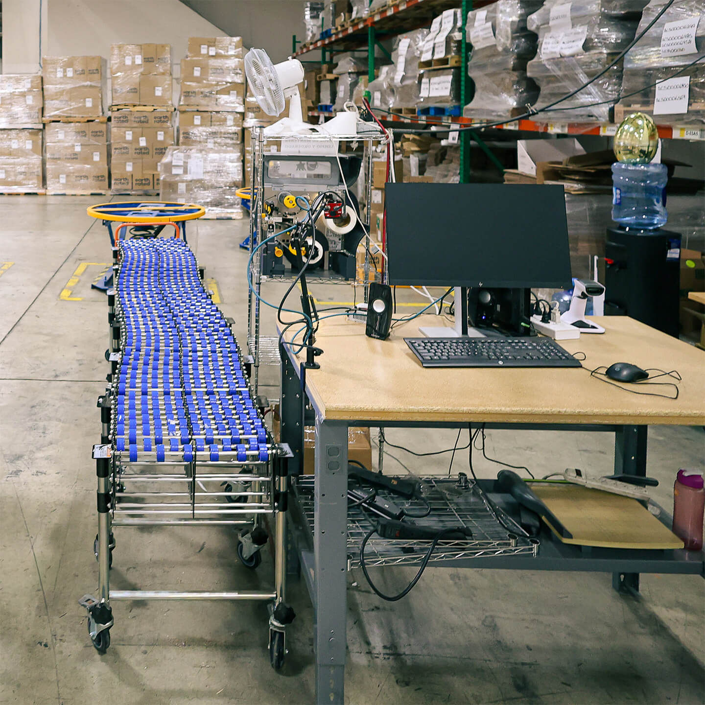 Warehouse packing station featuring a desktop computer and conveyor belt, symbolizing the seamless integration of technology and equipment for data-driven order fulfillment and real-time visibility.